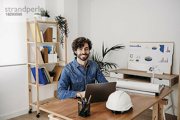 Glücklicher Ingenieur  der mit Laptop am Schreibtisch im Büro sitzt
