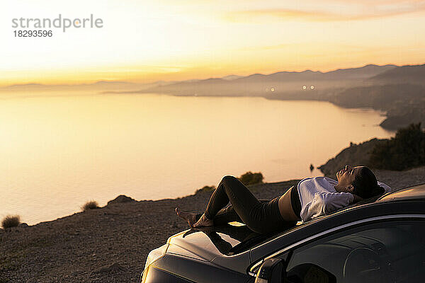 Woman with hands behind head relaxing on hood of car