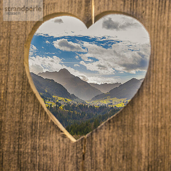 Mountains under sky seen through wooden heart shape