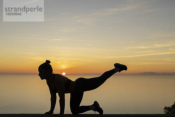 Silhouette einer Frau  die bei Sonnenuntergang Yoga praktiziert