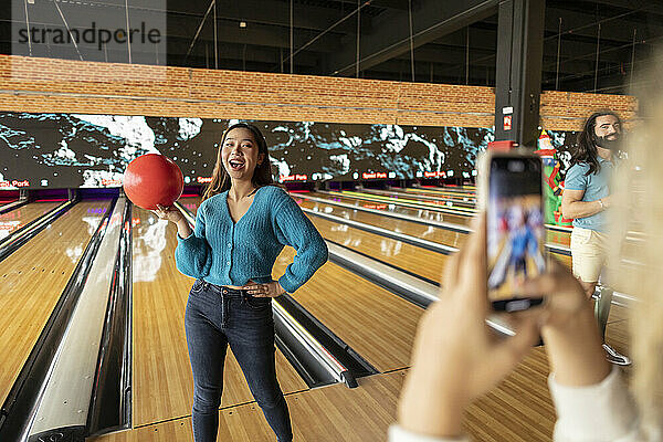 Frau fotografiert Freund mit Smartphone in Bowlingbahn
