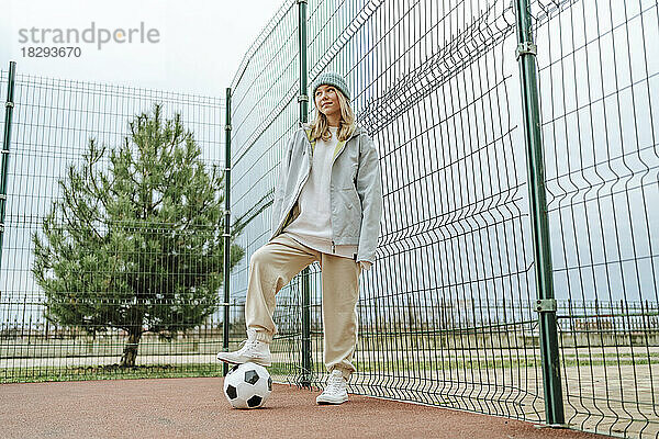 Teenager-Mädchen steht mit Fußball am Zaun am Spielplatz