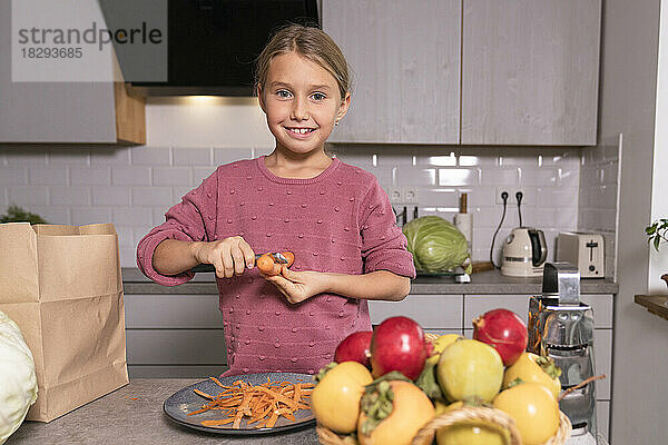 Porträt eines lächelnden Mädchens  das zu Hause in der Küche Karotten schält
