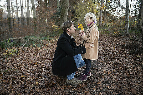 Vater und Tochter halten gelbes Ahornblatt im Herbstwald