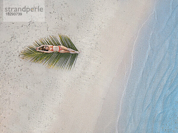 Frau liegt auf Palmblatt am Strand