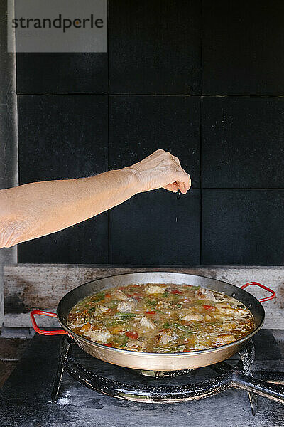 Frau streut Gewürze auf Paella in der Außenküche