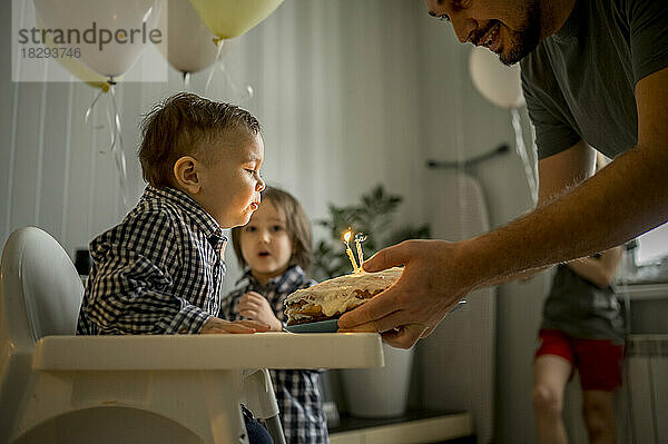 Vater und Sohn blasen Kerzen auf Kuchen und feiern Geburtstag mit der Familie zu Hause