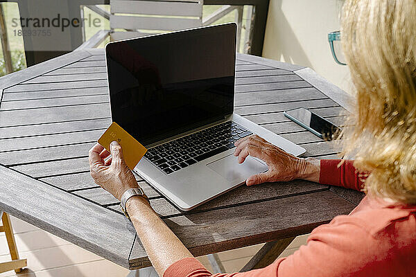 Frau mit Kreditkarte tätigt Online-Einkäufe per Laptop am Tisch
