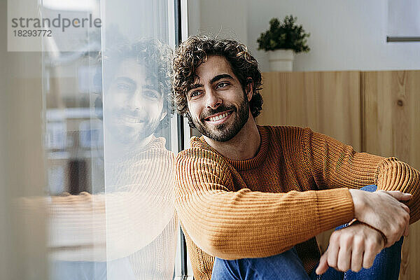 Happy young man leaning on glass window at home