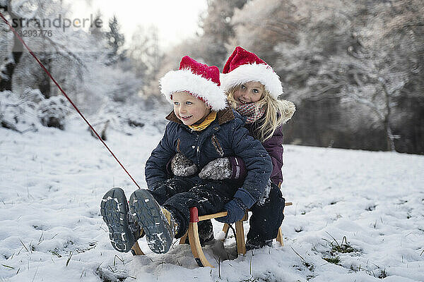 Lächelnder Bruder und Schwester sitzen auf Schlitten im Schnee