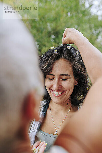 Frau schmückt im Park die Haare einer Freundin mit einer Blume