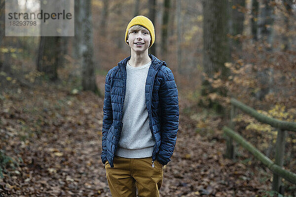 Lächelnder Junge mit den Händen in den Taschen im Herbstwald