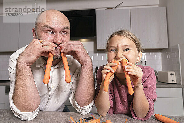 Vater und Tochter amüsieren sich zu Hause mit Karotten in der Küche