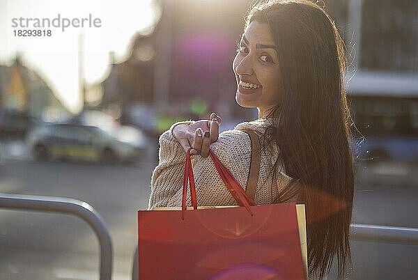 Glückliche junge Frau mit Einkaufstasche steht am Geländer