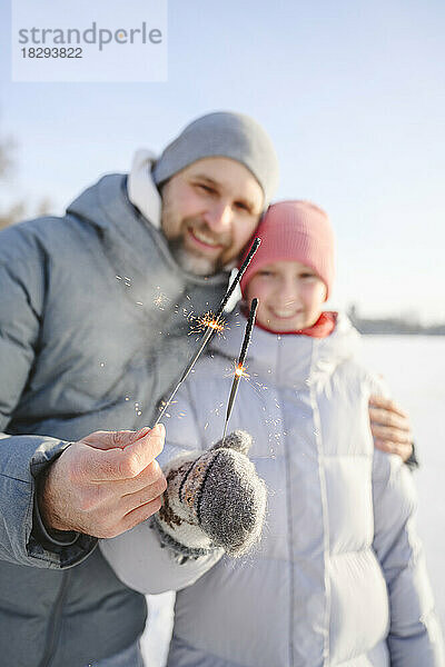 Glücklicher Vater und Tochter halten Wunderkerzen im Winter