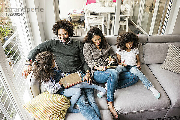 Glücklicher Vater mit Mutter und Töchtern  die zu Hause auf dem Sofa ein Buch lesen