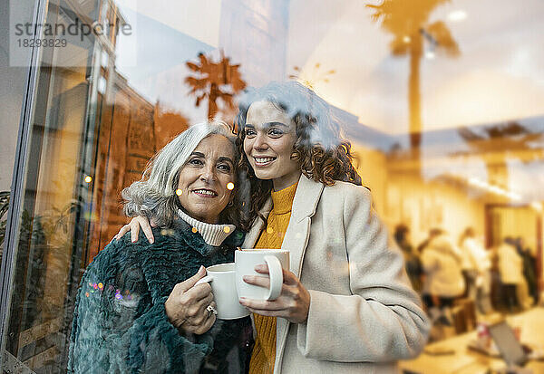 Glückliche junge Frau mit Großmutter  die eine Kaffeetasse durch Glas hält