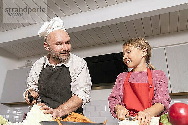 Vater und Tochter tragen Schürzen und bereiten zu Hause in der Küche gesunde Mahlzeiten zu