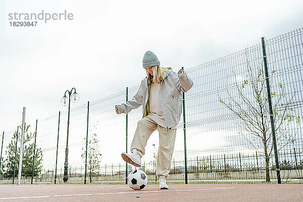 Fröhliches Teenager-Mädchen spielt mit Fußball auf dem Spielplatz