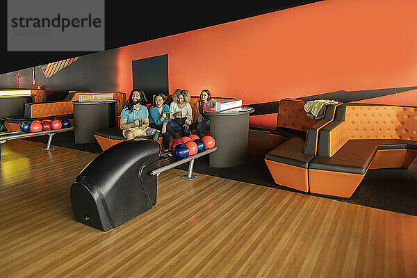 Multiracial friends sitting on sofa in bowling alley