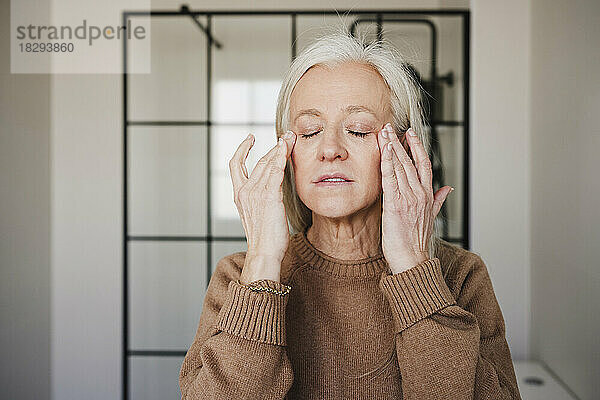 Reife Frau trägt zu Hause Feuchtigkeitscreme auf das Gesicht auf