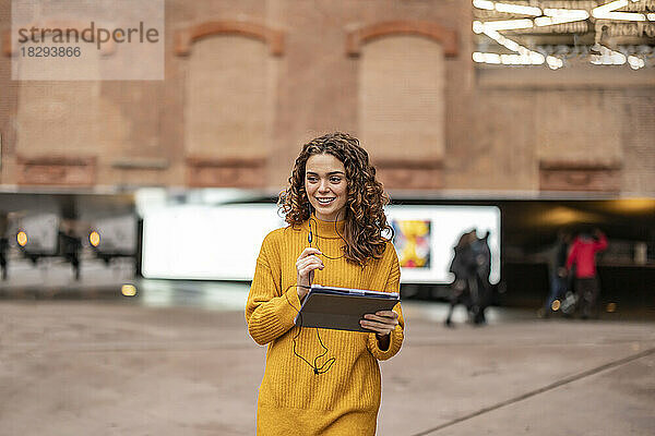 Glückliche junge Frau mit Tablet-PC  die vor dem Gebäude läuft
