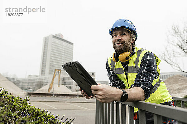 Lächelnder reifer Arbeiter mit Tablet-PC lehnt am Geländer