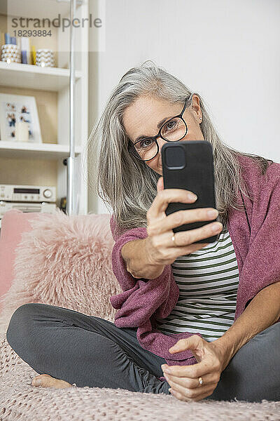 Reife Frau macht zu Hause ein Selfie mit dem Handy