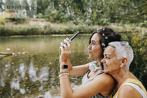 Junge Frau mit Freundin macht Selfie per Handy am Seeufer