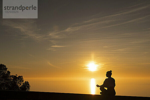 Silhouette einer Frau  die bei Sonnenuntergang Yoga macht