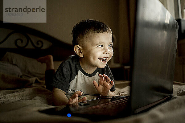 Happy boy with laptop lying on bed at home