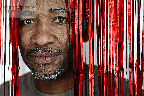 Mann blickt durch roten Lametta-Vorhang