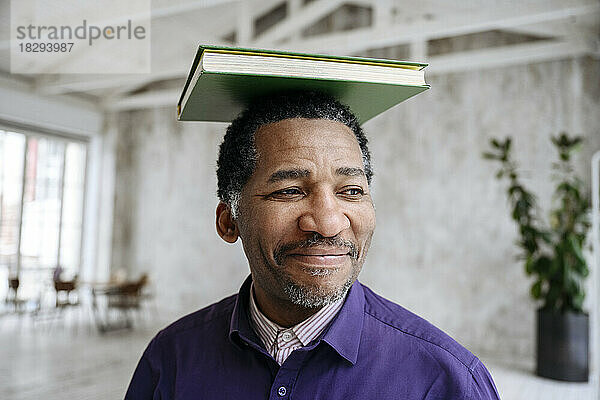 Lächelnder reifer Mann balanciert Buch auf dem Kopf
