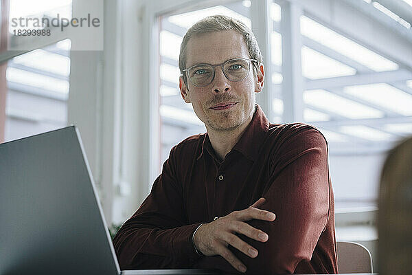 Lächelnder Geschäftsmann mit Laptop im Büro sitzend