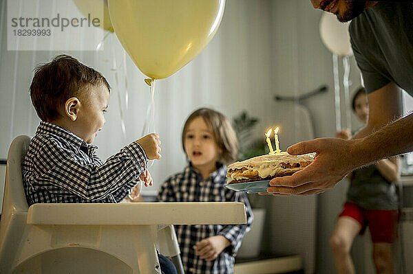 Vater hält Kuchen und feiert zu Hause den Geburtstag seines Sohnes