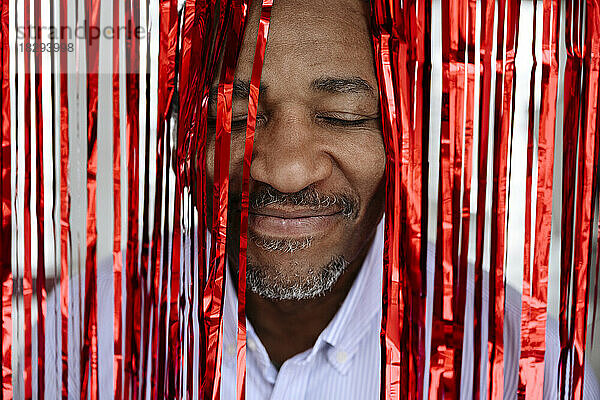 Smiling man with eyes closed amidst red tinsel curtain