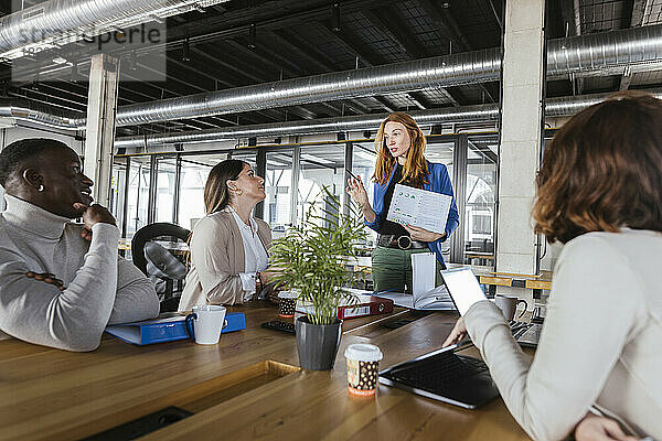 Rothaarige Geschäftsfrau diskutiert mit Kollegen im Coworking-Büro über ein Dokument