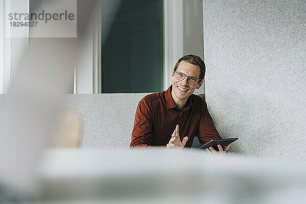 Glücklicher Geschäftsmann sitzt mit Tablet-PC im Büro