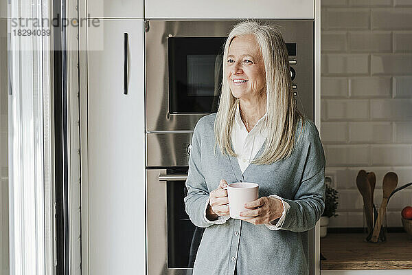 Glückliche reife Frau mit Kaffeetasse  die in der Küche steht