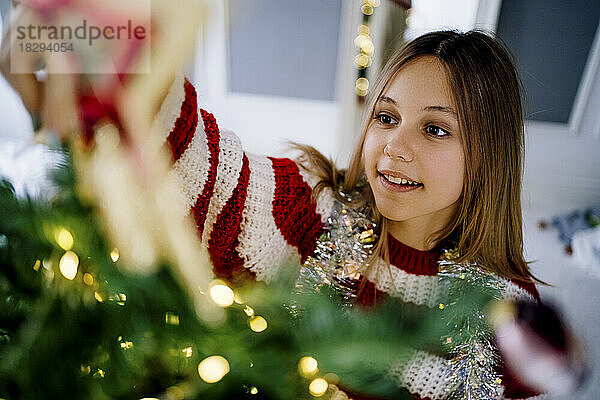 Mädchen schmückt Weihnachtsbaum zu Hause