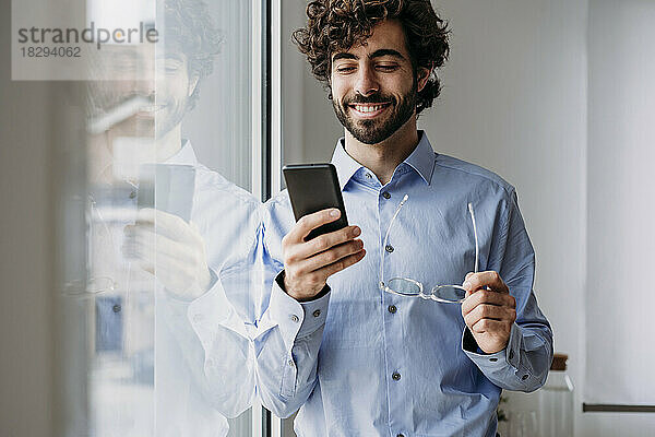 Lächelnder Geschäftsmann mit Smartphone und Brille im Büro