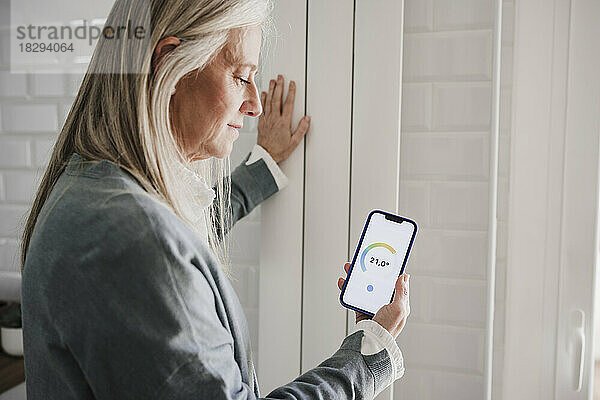 Frau nutzt Hausautomations-App auf Smartphone am Heizkörper