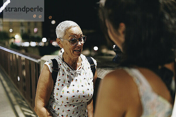 Ältere Frau unterhält sich nachts mit junger Freundin auf der Brücke