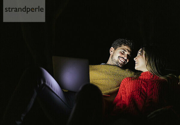 Happy couple using laptop at night smiling at each other
