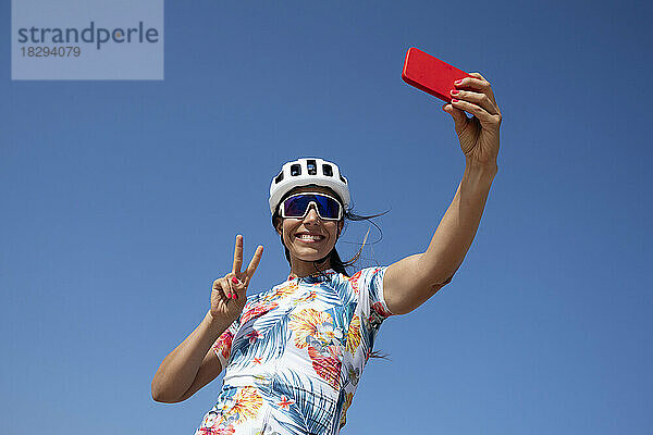 Glücklicher Radfahrer zeigt Friedensgeste und macht ein Selfie mit dem Smartphone