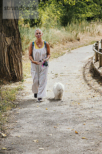 Ältere Frau geht mit Hund auf Fußweg im Park spazieren