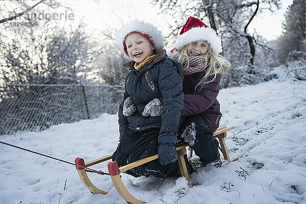 Glücklicher Bruder und Schwester sitzen auf Schlitten im Schnee
