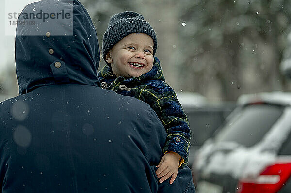 Fröhlicher Junge mit Strickmütze und Vater im Schnee