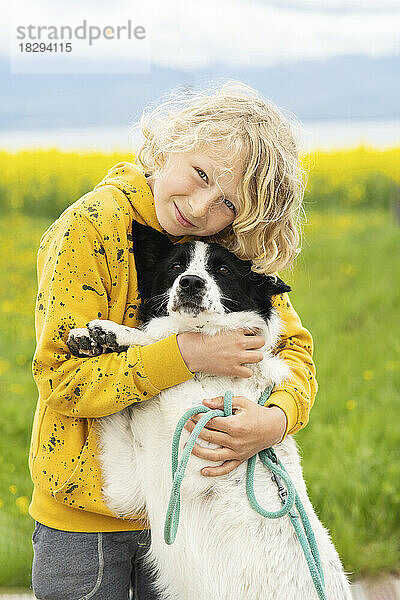 Fröhlicher Junge streichelt und umarmt den Border-Collie-Hund auf dem Feld