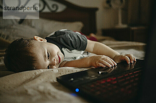 Junge liegt auf dem Bett und benutzt zu Hause Laptop